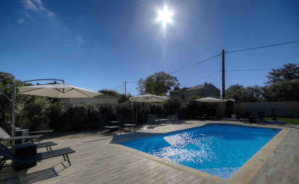 Piscine extérieure entourée de chaises longues et de parasols, sous un ciel bleu.