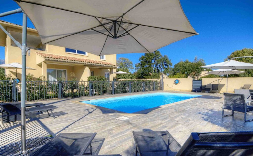 Piscine extérieure avec chaises longues et vue sur une maison moderne.