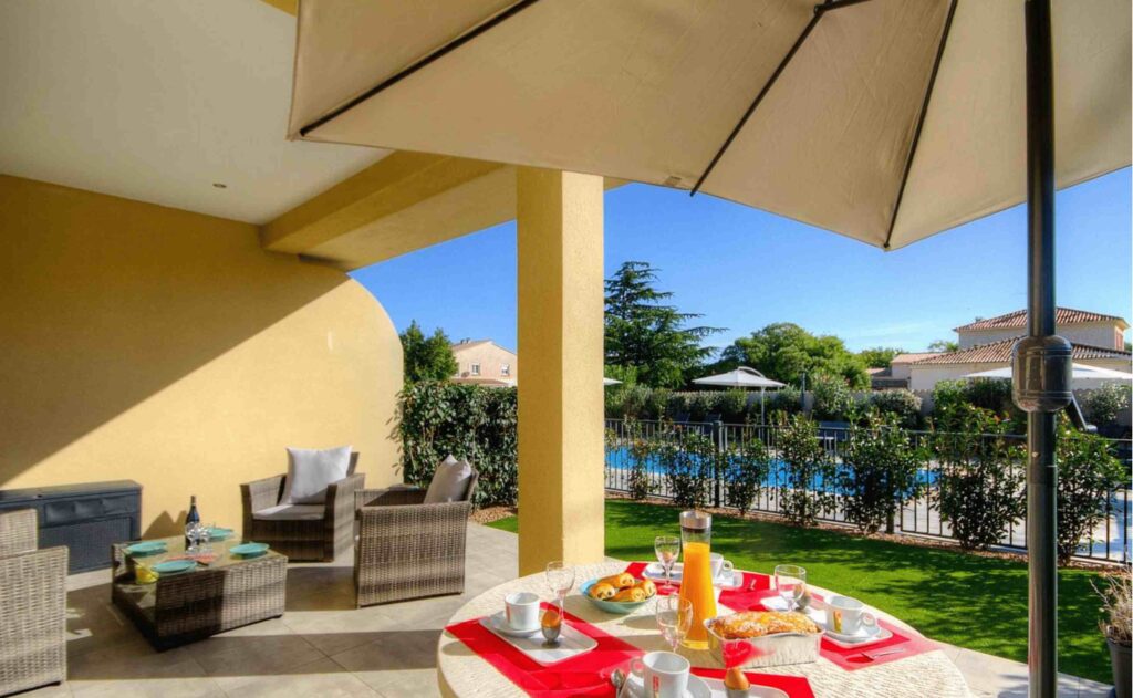Table de petit-déjeuner en terrasse avec vue sur la piscine et jardin.