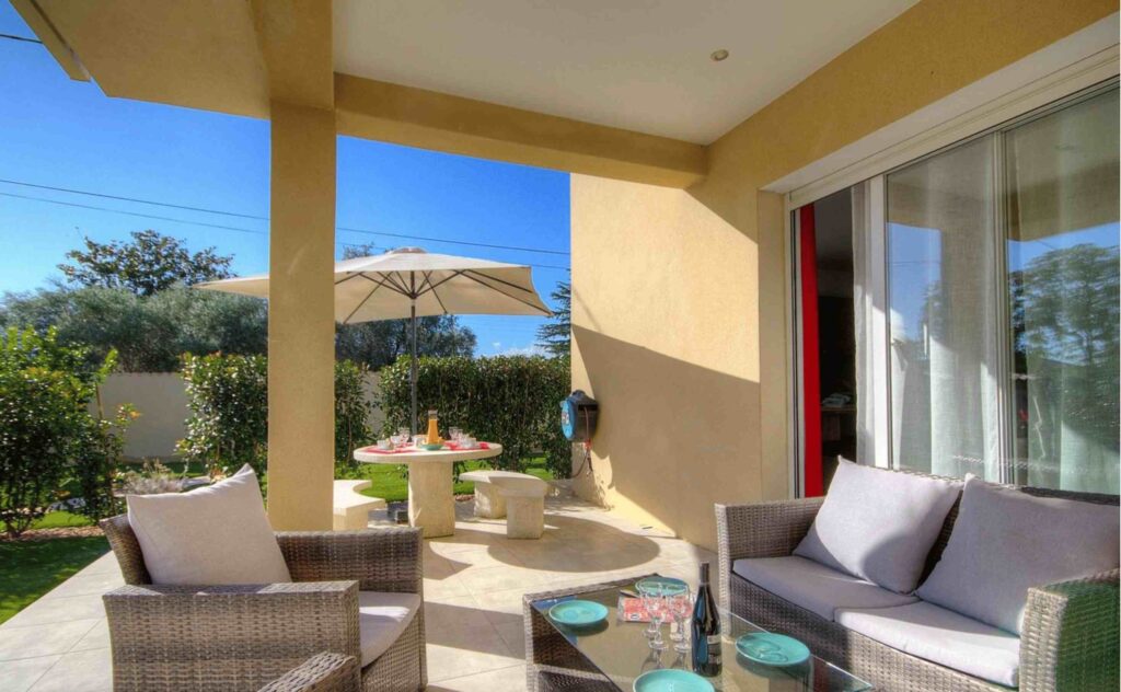 Terrasse couverte avec mobilier de jardin en rotin et vue sur le jardin.
