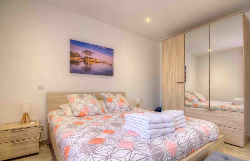 Chambre avec un lit double, un grand placard miroir, et des draps à motifs géométriques.