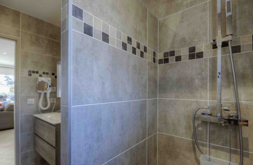 Salle de bain contemporaine avec carrelage mural en tons neutres, douche à effet pluie et miroir éclairé au-dessus d'un meuble-lavabo.